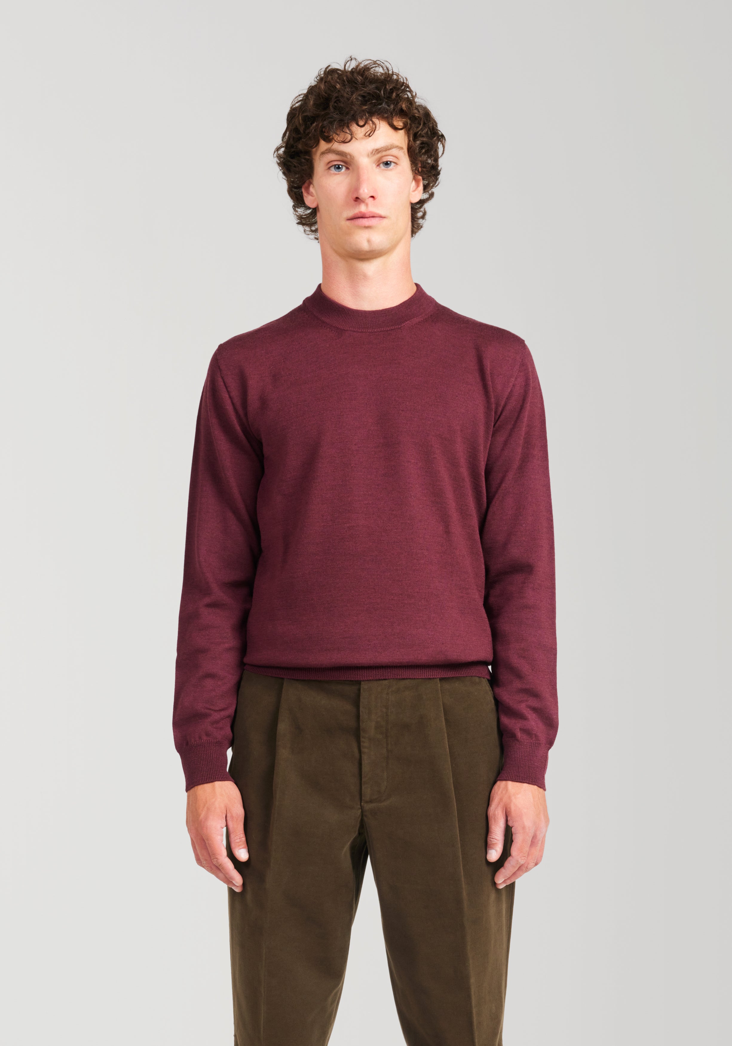 Man wearing a burgundy sweater and brown pants against a plain background
